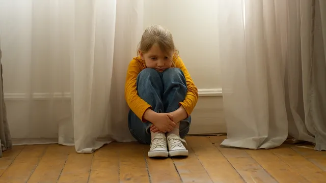 Een kind zit verdrietig in een huis.