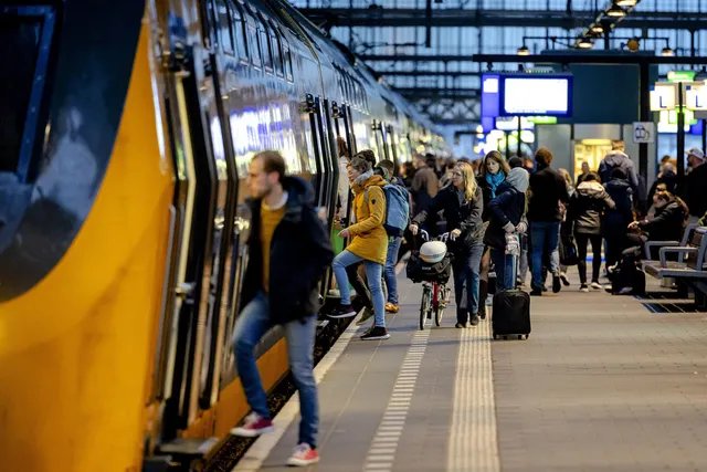 Op deze foto zie je een perron en een NS-trein, waar mensen instappen.