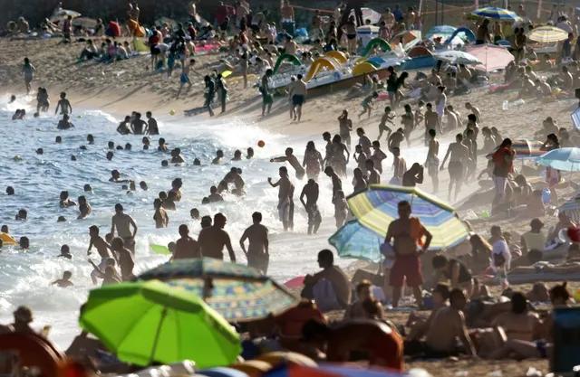 een drukbezocht strand in Spanje, waar het in de zomer ontzettend heet is. Een duidende afbeelding bij een artikel over hitte in Zuid-Europa en of we nog wel op vakantie kunnen naar het Zuiden.